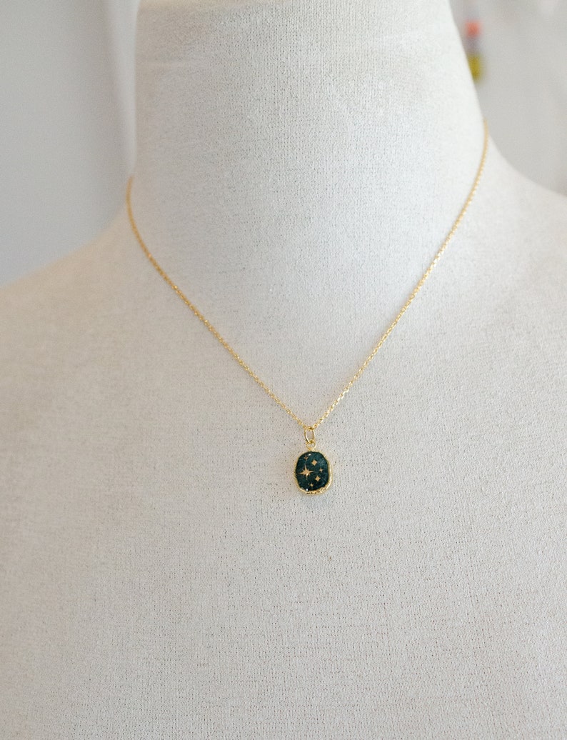 Op de afbeelding: Een gouden ketting met een donkergroene ovale hanger met een ontwerp van gouden sterren.