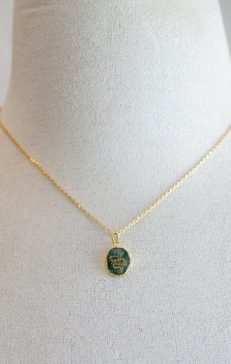 May include: A gold chain necklace with a green oval pendant featuring a gold snake design.
