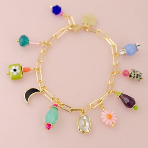 May include: A gold chain bracelet with multiple charms, including a flower, a crescent moon, a small bottle, a flower, a gemstone, and a charm with the letter "J".