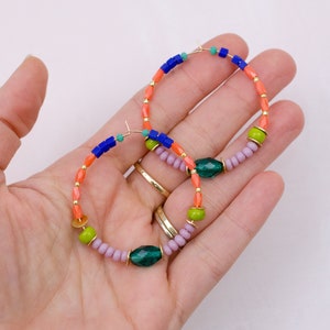 May include: A pair of hoop earrings with a multi-colored beaded design. The earrings feature orange, green, blue, and purple beads, as well as a larger green gemstone bead.