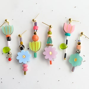 May include: Five pairs of colorful flower-shaped earrings with gold accents. Each earring features a variety of beads and charms, including flowers, leaves, and geometric shapes.