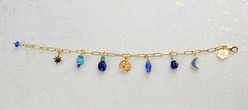 May include: Gold chain bracelet with blue and turquoise glass beads and charms, including a star, a crescent moon, a zodiac symbol, and a tag that says "Joy Always".