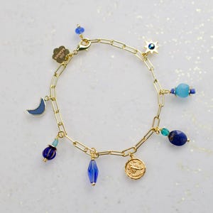 May include: Gold chain bracelet with blue and turquoise beads and charms, including a crescent moon, a star with an evil eye, a coin with a scorpion, and a crystal bead.