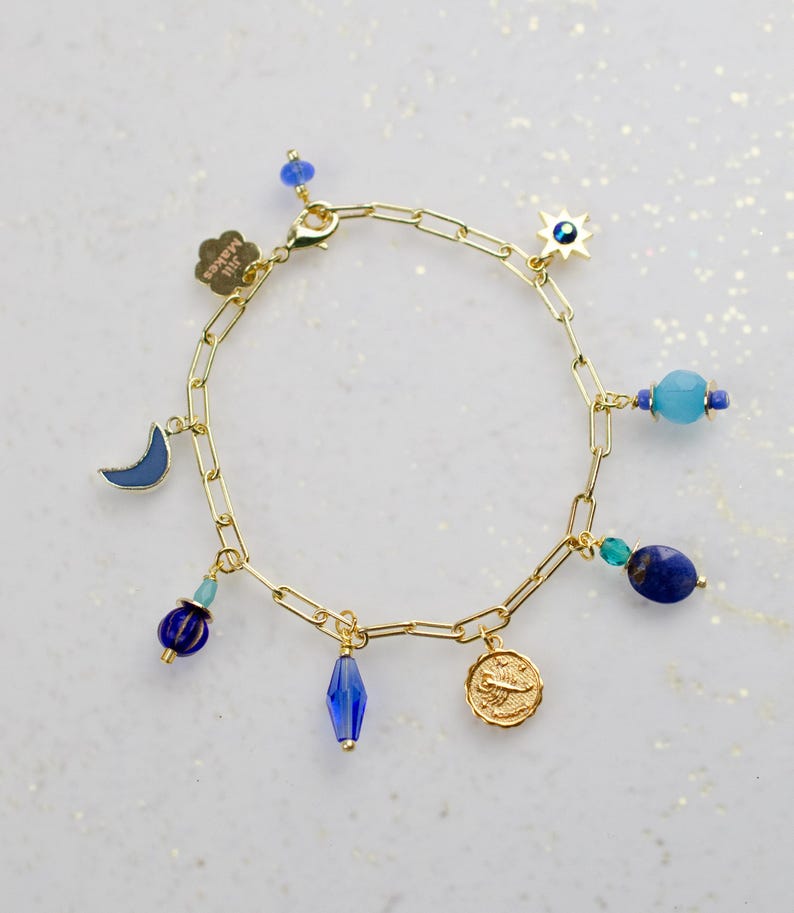 May include: Gold chain bracelet with blue and turquoise beads and charms, including a crescent moon, a star with an evil eye, a coin with a scorpion, and a crystal bead.