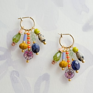 May include: A pair of gold hoop earrings with colourful beaded charms. The charms include green, yellow, blue, and purple beads in various shapes and sizes. The earrings have a bohemian style.