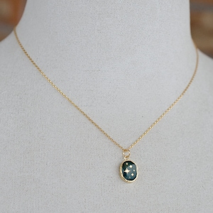Op de afbeelding: Een gouden ketting met een donkergroene ovale hanger met een gouden stervormig ontwerp.