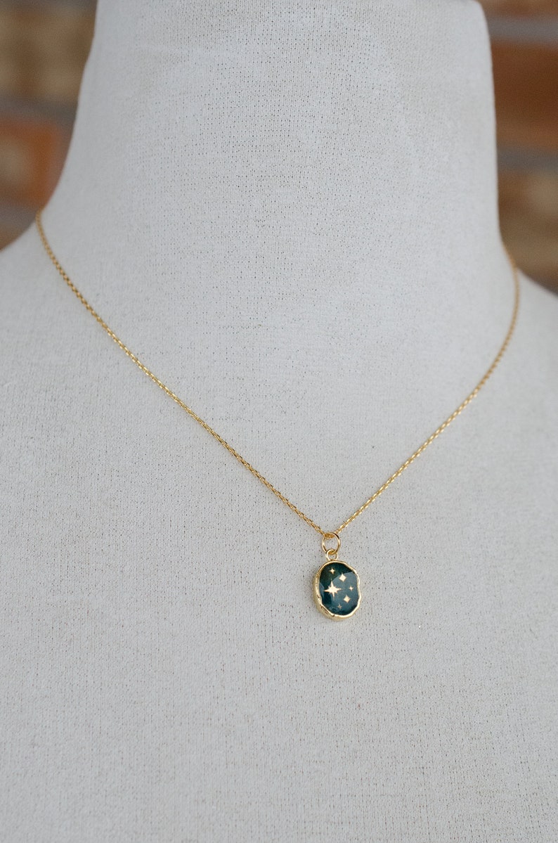 Op de afbeelding: Een gouden ketting met een donkergroene ovale hanger met een gouden stervormig ontwerp.