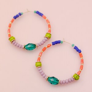 May include: A pair of hoop earrings with colorful beads and green crystal accents. The earrings are made of gold-toned metal and have a delicate, feminine look.