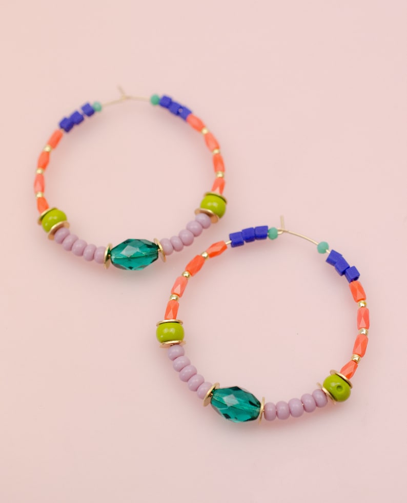 May include: A pair of hoop earrings with colorful beads and green crystal accents. The earrings are made of gold-toned metal and have a delicate, feminine look.
