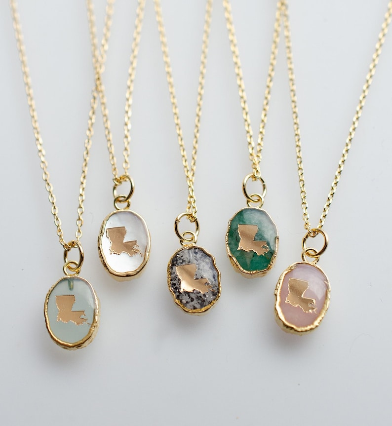 May include: Five gold necklaces with oval pendants featuring the state of Louisiana in gold on different colored backgrounds. The pendants are clear, green, gray, pink, and light blue.