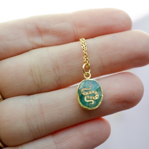 May include: A gold chain necklace with a green oval pendant featuring a gold snake design.