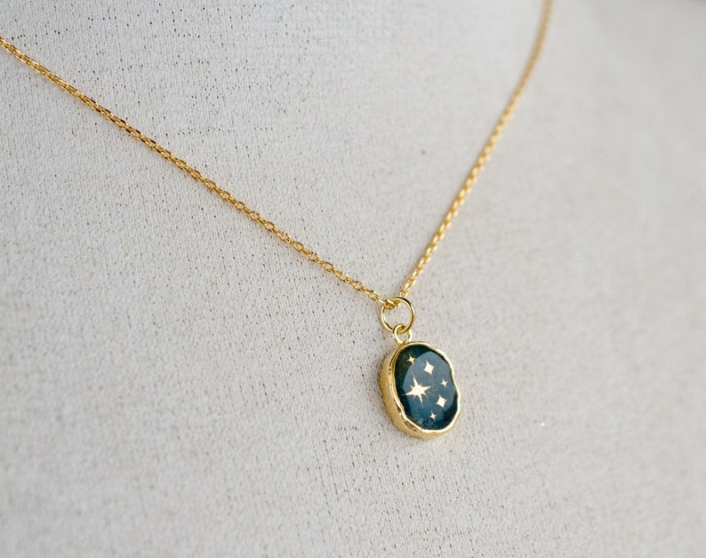 Op de afbeelding: Een gouden ketting met een donkergroene ovale hanger met gouden sterren.