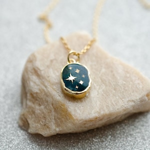Op de afbeelding: Een gouden ketting met een donkergroene ovale hanger met een gouden ster en kleinere gouden sterren op een donkergroene achtergrond.