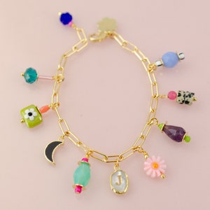 May include: A gold chain bracelet with multiple charms, including a crescent moon, a flower, a letter J, and various colored stones.