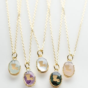 May include: Five gold necklaces with pendants featuring the outline of the state of Louisiana in gold on different colored stones. The stones are green, pink, white, purple, and light green.