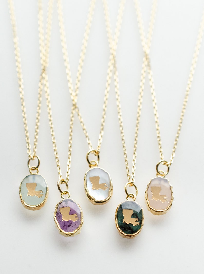 May include: Five gold necklaces with pendants featuring the outline of the state of Louisiana in gold on different colored stones. The stones are green, pink, white, purple, and light green.