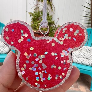 May include: Red glitter Mickey Mouse shaped ornament with a silver glitter trim. The ornament has a silver loop for hanging.