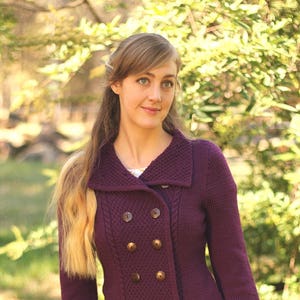 Może przedstawiać: Kobieta w fioletowym kardiganie zapinanym na guziki z dwoma rzędami guzików i niebieskich dżinsach.