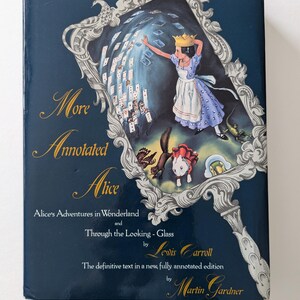 May include: A blue book cover with a mirror image of Alice in Wonderland. The title is "More Annotated Alice" with the text "Alice's Adventures in Wonderland and Through the Looking-Glass by Lewis Carroll. The definitive text in a new, fully annotated edition by Martin Gardner."