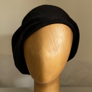 May include: A black knit beret hat on a wooden mannequin head.