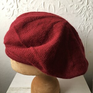 May include: A deep red knitted beret, displayed on a wooden mannequin head.