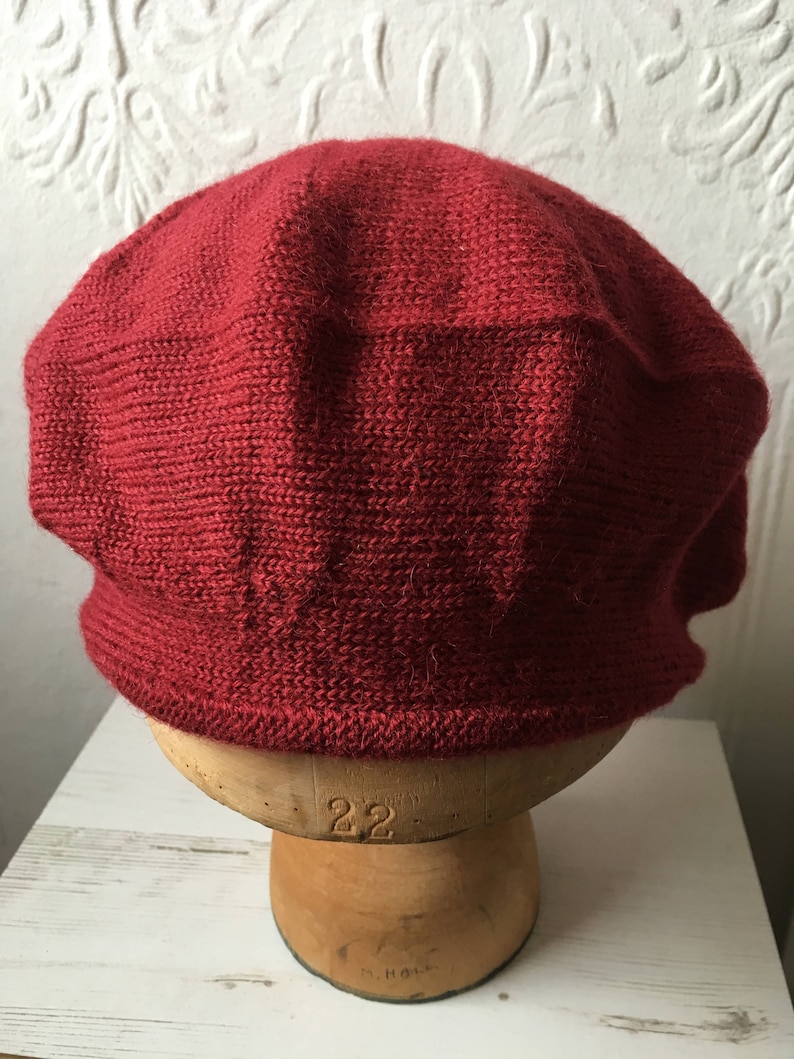 May include: A red knitted beret on a mannequin head. The beret is made of a soft, textured yarn.