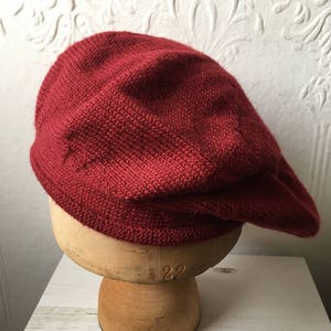 May include: A deep red knitted beret, displayed on a wooden hat form.