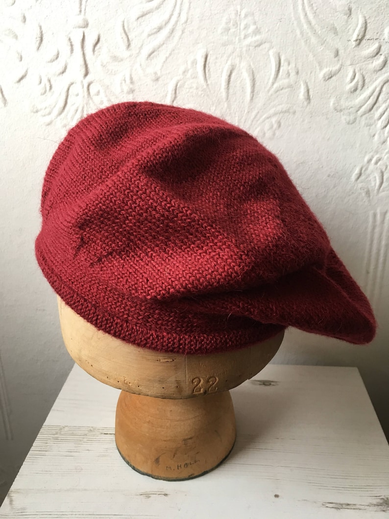 May include: A deep red knitted beret, displayed on a wooden hat form.