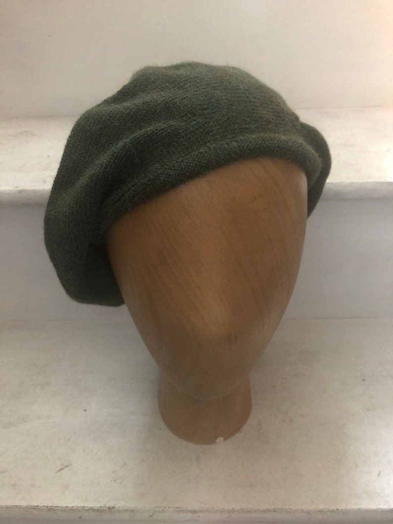 May include: A dark green knitted beret. The beret is made of a soft, textured fabric.