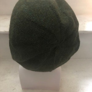 May include: A dark green knitted beanie hat. The hat is made of a soft, textured fabric and has a simple, classic design.