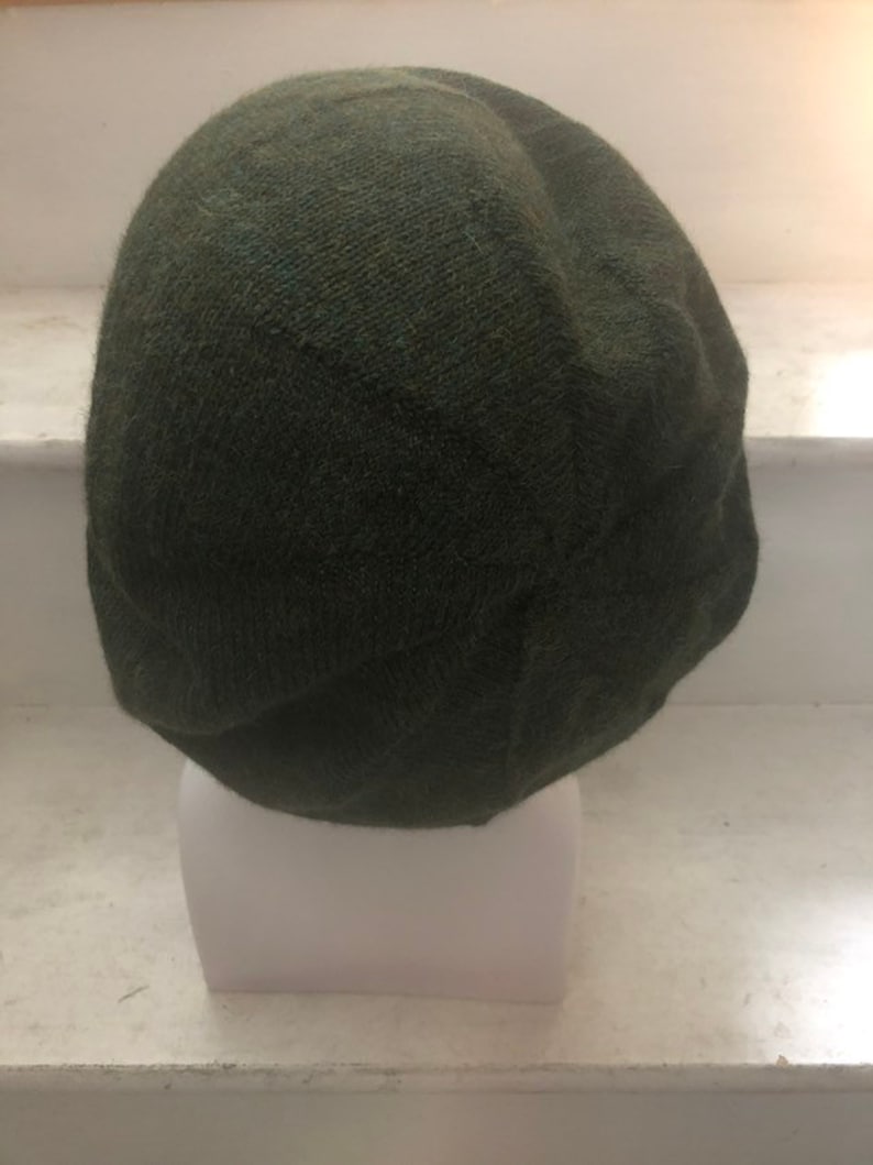 May include: A dark green knitted beanie hat. The hat is made of a soft, textured fabric and has a simple, classic design.
