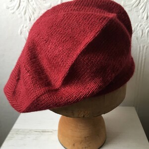 May include: A deep red knitted beret, displayed on a wooden hat form.