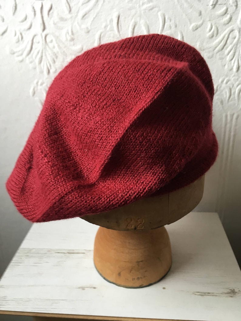 May include: A deep red knitted beret, displayed on a wooden hat form.