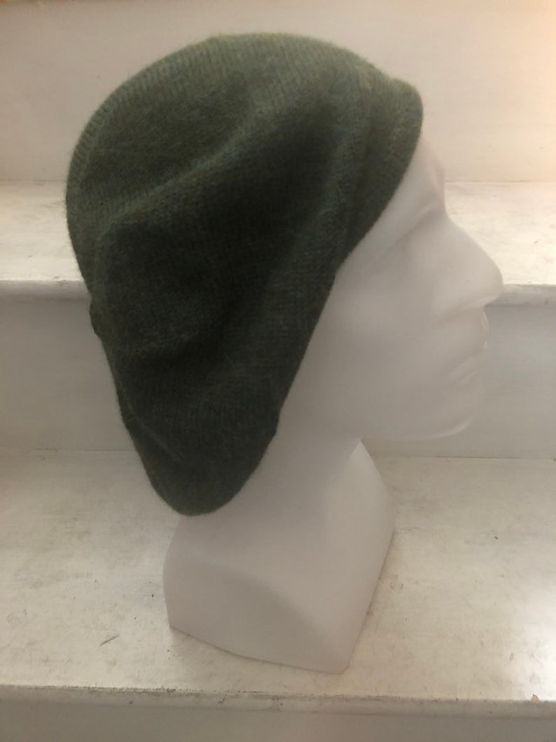 May include: A dark green knitted beret. The beret is made of a soft, fuzzy material and has a classic, round shape.