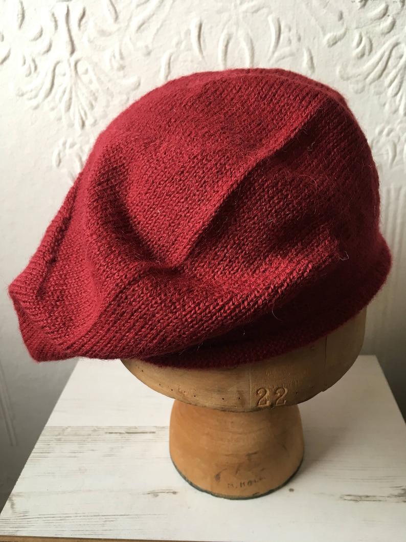May include: A deep red knitted beret, sitting on a wooden hat form.