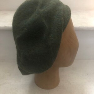 May include: A dark green knitted beret hat. The hat is on a brown mannequin head.
