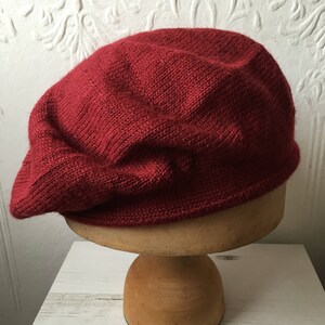 May include: A deep red knitted beret, displayed on a wooden hat stand.