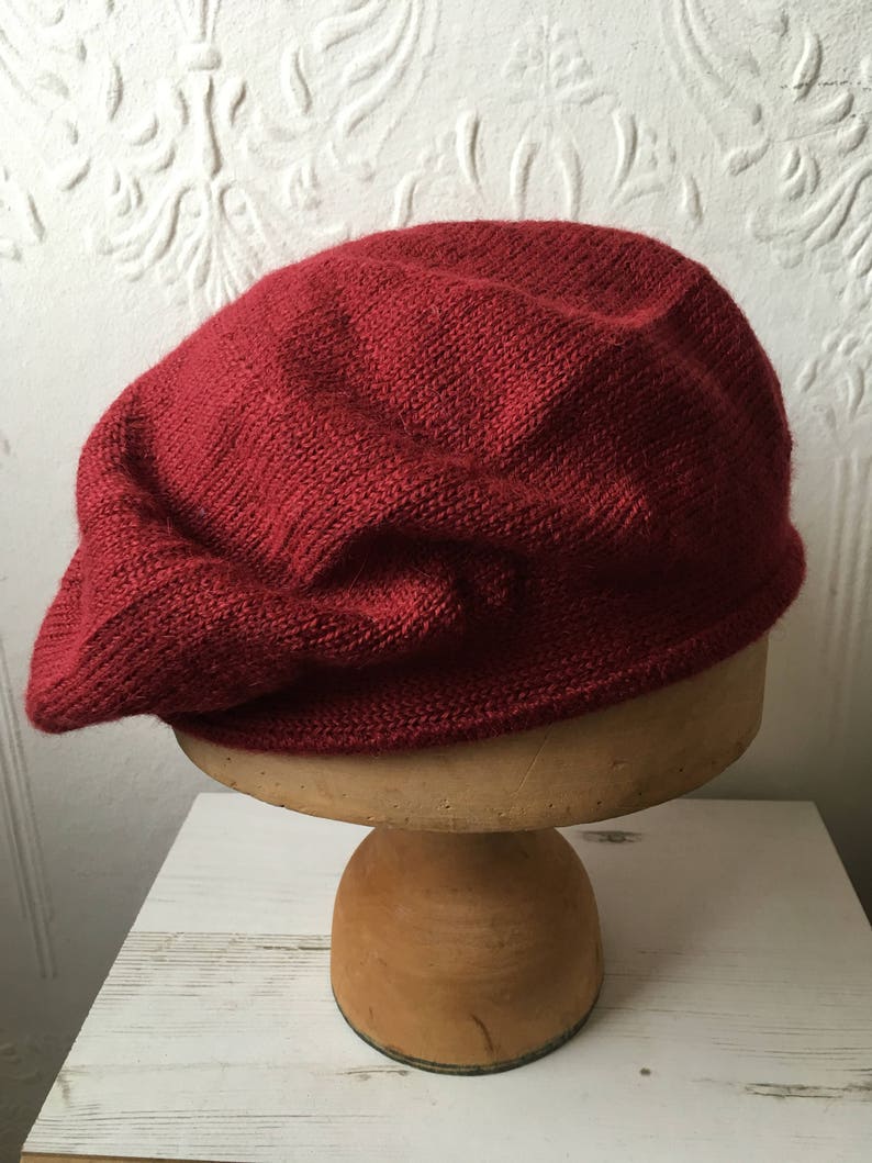May include: A deep red knitted beret, displayed on a wooden hat stand.