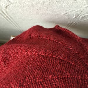 May include: Close-up of a red knitted fabric with a textured pattern.