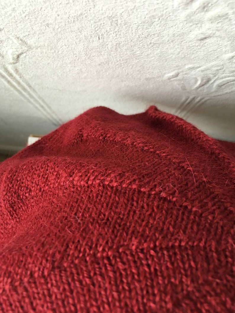 May include: Close-up of a red knitted fabric with a textured pattern.