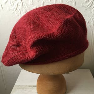 May include: A red knitted beret on a wooden display stand.