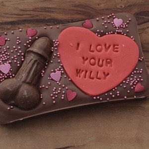 K&ouml;nnte beinhalten: Eine Schokoladentafel mit einem roten herzf&ouml;rmigen Bonbon darauf. Der Bonbon hat die Aufschrift "I love your willy". Die Schokoladentafel ist mit rosa Streuseln und Herzen verziert.