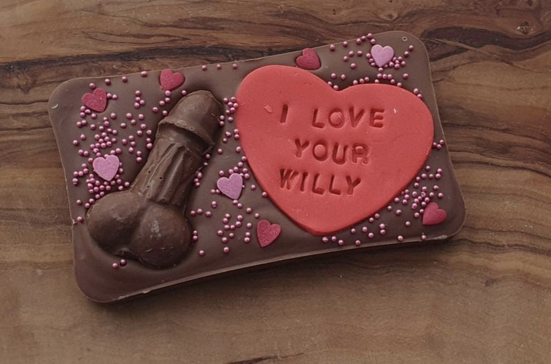 K&ouml;nnte beinhalten: Eine Schokoladentafel mit einem roten herzf&ouml;rmigen Bonbon darauf. Der Bonbon hat die Aufschrift "I love your willy". Die Schokoladentafel ist mit rosa Streuseln und Herzen verziert.