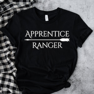 May include: Black t-shirt with white text that reads "Apprentice Ranger" with an arrow pointing to the right.