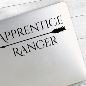 May include: A silver laptop with the words "APPRENTICE RANGER" in black, with a black arrow pointing left. The text is centered and the arrow is a straight line through the words.