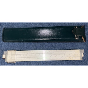 May include: A white plastic slide rule featuring a clear sliding cursor with metal end caps, accompanied by a dark green leather protective case with a flap closure and a metal snap button fastener, presented as a set for mathematical calculation.
