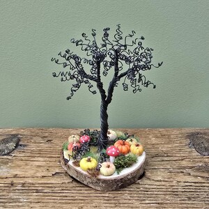 May include: A handcrafted wire tree sculpture with a twisted trunk and curly branches. The tree sits on a wooden base surrounded by miniature pumpkins and mushrooms in shades of orange, yellow, and red. The base is approximately 4 inches in diameter.