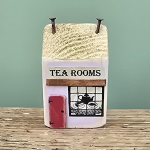 May include: A wooden tea room sign with a white background and black lettering that reads "TEA ROOMS". The sign has a red door and a window with a black silhouette of a teapot and teacups.