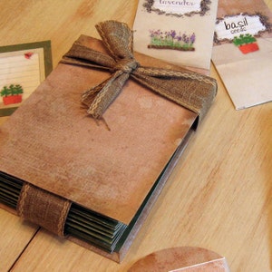 May include: A brown paper-covered journal with a hessian ribbon tied around it. The journal is sitting on a wooden surface with three small envelopes labelled "lavender", "basil seeds", and "seeds".