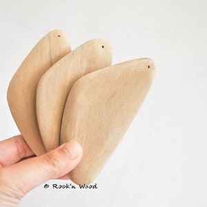 May include: Three natural wood, teardrop-shaped pendants with a hole at the top. The pendants are stacked on top of each other and are held in a hand.